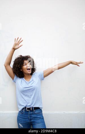 Portrait cheerful young african american woman with arms raised by white background Stock Photo