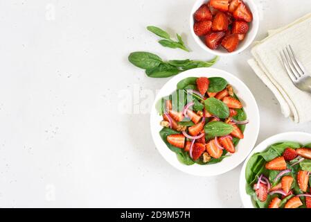 Fruit salad with strawberry, basil and walnut on light background with copy space. Fresh strawberries slices in  bowl. Top view, flat lay. Stock Photo