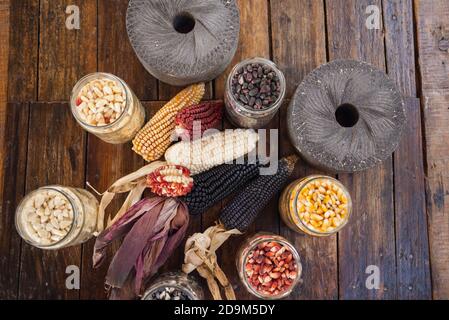 Top view of a colorful corn ears and kernels in glass jars with grinding stones on a wooden table Stock Photo