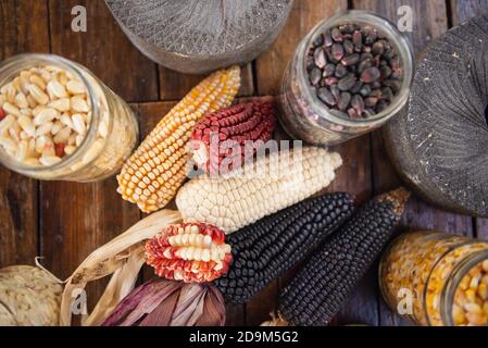Top view of a colorful corn ears and kernels in glass jars with grinding stones on a wooden table Stock Photo