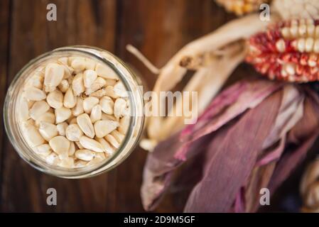 Selective focus shot of dried corn kernels in a glass jar with corn leaves on the background Stock Photo