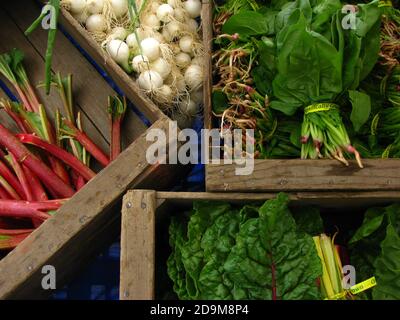 Closeup shot of white onions, spinach, and rainbow chard displayed on wooden crates Stock Photo