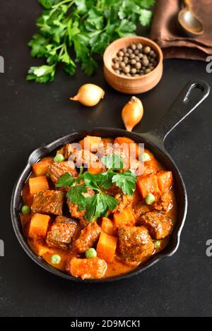 Beef stew with potatoes and carrots in tomato sauce on black stone background Stock Photo