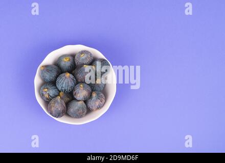 White bowl with whole ripe figs on a blue background Copy space. Stock Photo