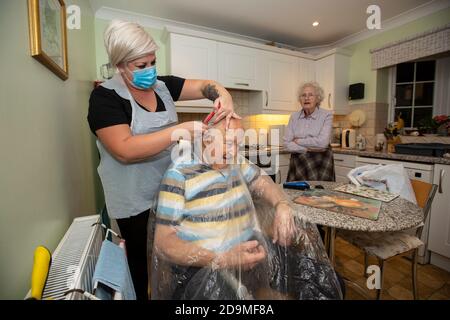 Elderly man in his eighties having his hair cut by a hairdresser wearing PPE as protection against coronavirus whilst at working remotely, England, UK Stock Photo