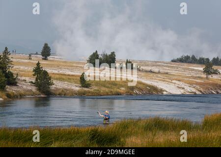 A fly fisherman on the Firehole River in Yellowstone National Park in Wyoming.  Steam rises from the Midway Geyser Basin behind. Stock Photo