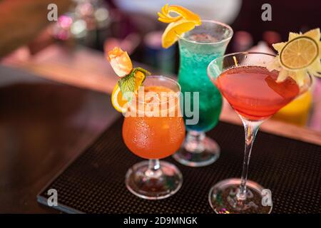 Colorful cocktails on bar counter. Tropical cocktails on restaurant table, ready to serve. Nightlife party, bar drink background, blurred bottles Stock Photo