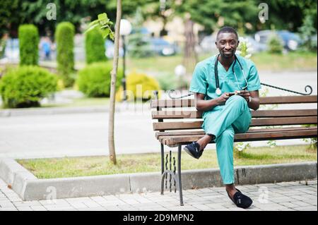 Portrait of African male doctor with stethoscope wearing green coat with mobile phone at hand. Stock Photo