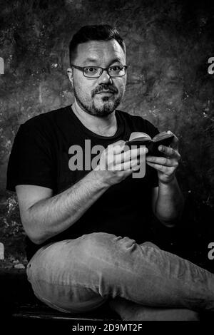 Mature bearded man dressed in t-shirt reading small book studio portrait. Stock Photo
