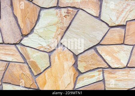 Close-up of a wall tiled with sandstone tiles. Design, construction. Chaotic stone mosaic. Natural stone. A versatile background for different purpose Stock Photo
