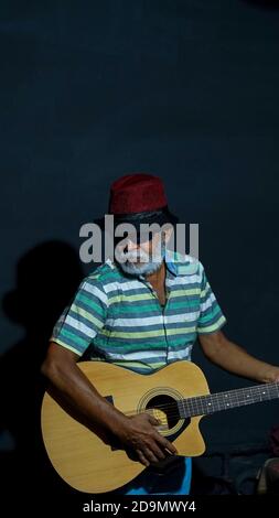Bearded Asian senior man wearing a hat and sunglasses posing at the camera with a guitar Stock Photo