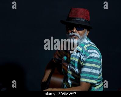 Bearded Asian senior man wearing a hat and sunglasses posing at the camera with a guitar Stock Photo