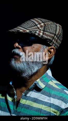 Bearded Asian senior man wearing a hat and sunglasses isolated on a black background Stock Photo