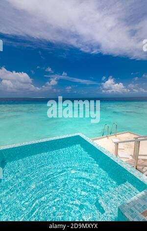 Infinity swimming pool with sea and ocean view on blue sky background. Luxury infinity pool over amazing turquoise lagoon and ladder into the water Stock Photo
