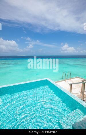 Infinity swimming pool with sea and ocean view on blue sky background. Luxury infinity pool over amazing turquoise lagoon and ladder into the water Stock Photo
