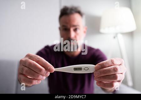 Sick Man With Fever Holding Thermometer Showing High Temperature Stock Photo