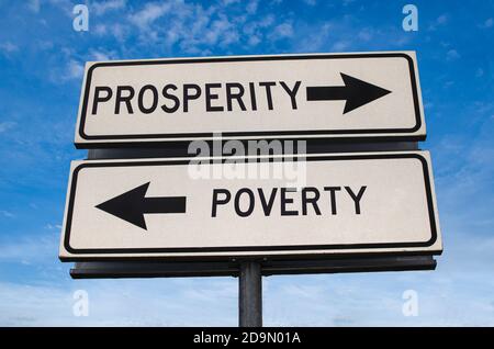 Poverty versus prosperity white arrow road sign on blue sky background. White two street signs with arrow on metal pole with word. Directional road.