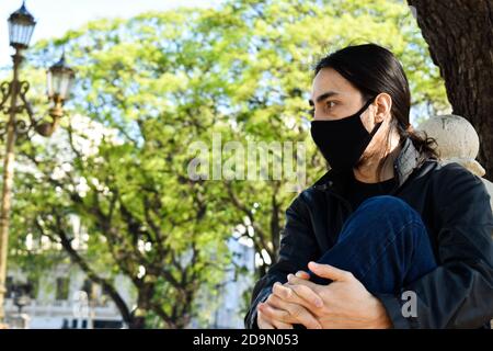 young man thinking sitting on the balcony railing wearing mask Stock Photo