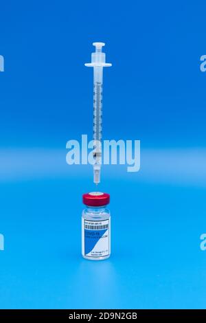 Vertical image of a COVID-19 vaccine vial with a syringe inserted into it upright on a blue background Coronavirus concept Stock Photo