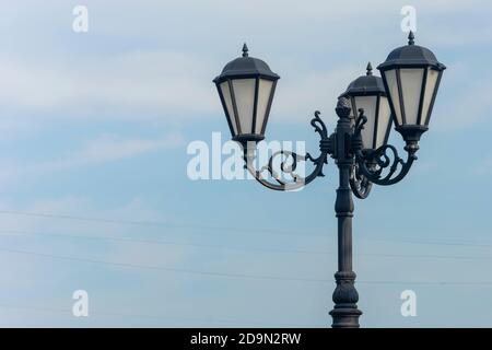 Retro street lamp against the blue sky. An old-fashioned wrought iron lamppost with beautiful decorations. Stock Photo