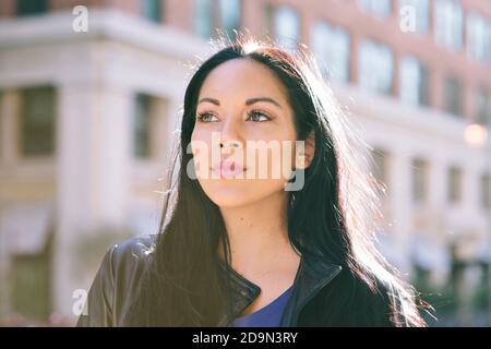Latina Female stands with strength while looking off to the left - Goal Achievement - Big City - Daytime Stock Photo