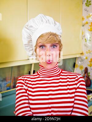 1970s BLONDE HOUSEWIFE WEARING CHEF’S HAT RED AND WHITE TURTLE NECK TOP EYES WIDE OPEN MAKING FUNNY FACIAL EXPRESSION IN KITCHEN - kg5584 HAR001 HARS FACIAL COMMUNICATION BLOND COMIC NECK JOY LIFESTYLE FEMALES HOME LIFE COPY SPACE LADIES PERSONS WHISTLING EXPRESSIONS AMAZED WIDE EYE CONTACT HOMEMAKER BUG-EYED HUMOROUS HOMEMAKERS HEAD AND SHOULDERS DISCOVERY AND EXCITEMENT COMICAL HOUSEWIVES OCCUPATIONS COMEDY STYLISH TURTLE WIDE-EYED ASTONISHED EXCLAMATION MID-ADULT MID-ADULT WOMAN TOQUE AMAZEMENT CAUCASIAN ETHNICITY CHEF'S FOOD PREPARATION HAR001 OLD FASHIONED PUCKERED Stock Photo