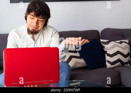 Hispanic young man in casual clothes brainstorming at a distance with a laptop on a sofa with a calm and thoughtful attitude Stock Photo