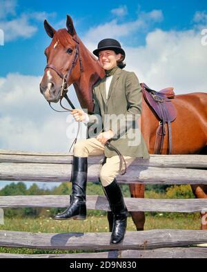 1970s WOMAN WEARING BOWLER STYLE HAT JACKET RIDING BREECHES BOOTS SITTING ON RAIL FENCE HOLDING REINS HORSE WITH ENGLISH SADDLE - kh3500 HAR001 HARS PLEASED JOY LIFESTYLE RELIGION FEMALES TWEED RURAL BOWLER HEALTHINESS COPY SPACE FRIENDSHIP FULL-LENGTH LADIES PERSONS SADDLE ATHLETIC CONFIDENCE TRANSPORTATION ENGLISH RAIL RIDER REINS HAPPINESS MAMMALS CHEERFUL ADVENTURE EASTERN LOW ANGLE PRIDE ON SMILES ENGLISH SADDLE JOYFUL STYLISH EQUINE COOPERATION MAMMAL YOUNG ADULT WOMAN BREECHES CAUCASIAN ETHNICITY EQUESTRIAN HAR001 OLD FASHIONED Stock Photo