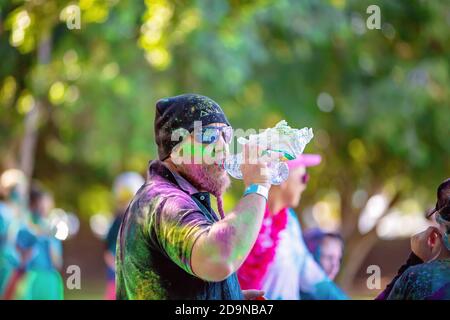 MACKAY, QUEENSLAND, AUSTRALIA - JUNE 2019: Unidentified bearded man splattered with powder having a drink during Color Frenzy Fun Run Stock Photo