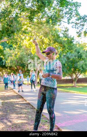 MACKAY, QUEENSLAND, AUSTRALIA - JUNE 2019: Unidentified woman sprinkles yellow powder over herself in Color Frenzy Fun Run Stock Photo