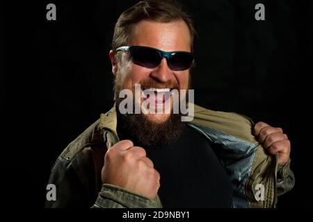 Emotional bearded man in sunglasses dressed in leather jacket is happy to win studio portrait Stock Photo