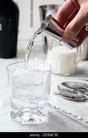 Man's hand pouring vodka from a jigger into a glass with ice. White Russian cocktail preparation Stock Photo