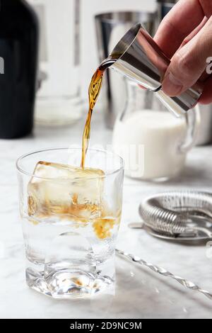 Man's hand pouring coffee liqueur into a glass with ice. White Russian cocktail preparation Stock Photo