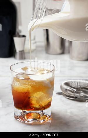 White Russian cocktail preparation. Pouring cream into the glass Stock Photo