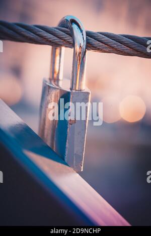 close-up of a padlock hanging on a wire on a bridge in the old harbor of La Rochelle at sunset. beautiful bright and blurred background Stock Photo
