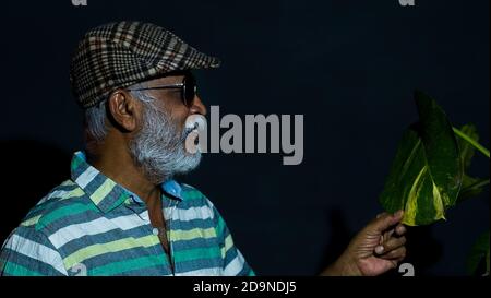 Side view of a bearded Asian senior man wearing a hat and sunglasses isolated on a black background Stock Photo