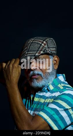 Vertical shot of a bearded Asian senior man wearing a stylish hat isolated on a black background Stock Photo