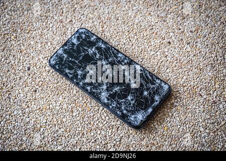 Closeup of Modern mobile smart phone with broken, cracked screen on stone floor background. Select focus Stock Photo