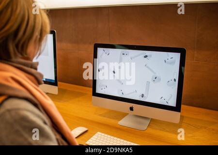 Paris, France - Nov 16, 2019: Side view of woman looking at the latest Apple Computers iMac 27 21 inch personal computers featuring advertising on the 5k screen for the new Airpods Pro headphones Stock Photo