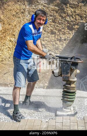 A Caucasian construction worker compacting soil using a tamping rammer machine Stock Photo