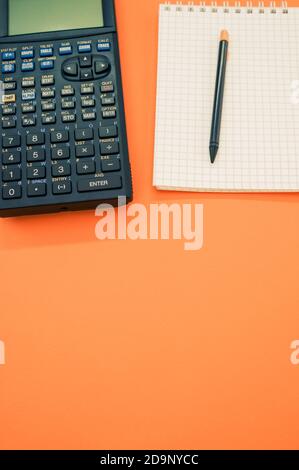 A top view closeup of a graphing calculator and a pen on a notepad  isolated on an orange background Stock Photo