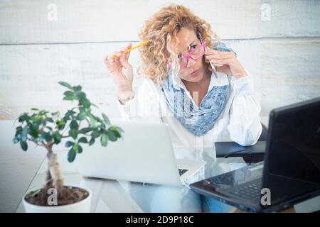 Modern technology job people - adult caucasian woman at office doing a phone call - laptop computer on the workplace desktop - businesswomn and same right female concept Stock Photo