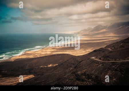 Travel in amazing scenic places concept with white car on a off road and beautiful landscape in background with coastline, beach, ocean, mountains and sky with clouds - vacation in incredible places concept Stock Photo