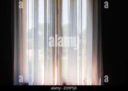 White semi-sheer curtains hanging  from a decorative curtain rod on tall double windows. Stock Photo