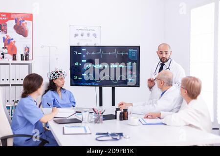 Doctor using headset with sensors on consciousness female nurse during neuroscience research. Monitor shows modern brain study while team of scientist adjusts the device. Stock Photo