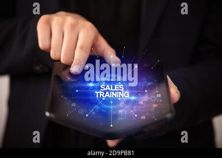 Businessman holding a foldable smartphone with SALES TRAINING inscription, new business concept