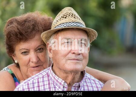 marriage of older people. him in a straw hat taking a picture together while she hugs him from behind and smiles Stock Photo
