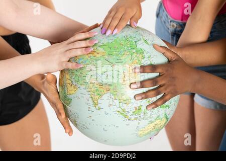 A large globe with all continents is supported by female hands of various races, symbolizing unity, acceptance and racial tolerance. Stock Photo