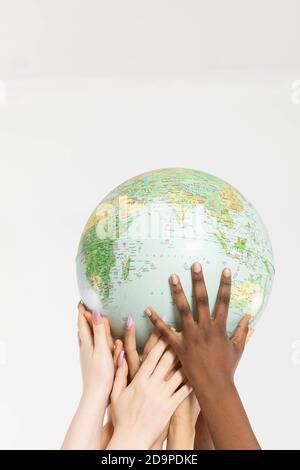 A large globe with all continents is supported by female hands of various races, symbolizing unity, acceptance and racial tolerance. Stock Photo