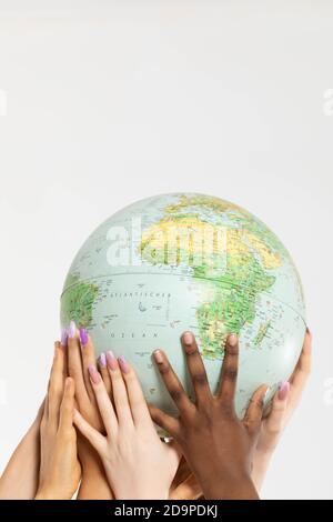 A large globe with all continents is supported by female hands of various races, symbolizing unity, acceptance and racial tolerance. Stock Photo